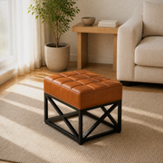 Oak living room angle | saddle tan leather ottoman showing its stitched top, side depth, and black X-base