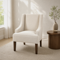 Living room hero | cream polyester swoop-arm accent chair beside a round walnut side table, tall window at left