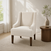 Living room hero | cream polyester swoop-arm accent chair beside a round walnut side table, tall window at left