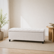Room 1 | Ivory button-tufted storage bench in a warm white room with a leafy plant by the bright window, light wood floor, and round wood table