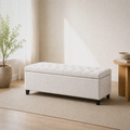 Room 1 | second three-quarter angle of the ivory button-tufted storage bench in the warm white room with a leafy plant, round wood table, and light wood floor