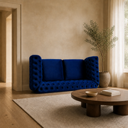 Scale | Navy-blue button-tufted rolled-arm loveseat beside a full-height doorway in a warm living room