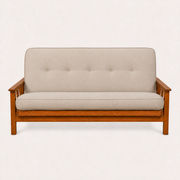 Front | Linen stone futon straight on in an off-white studio, with five back tufts, amber Barbados wood and three-slat arms