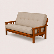 Studio | Linen stone futon from a 55-degree front-right angle, showing the full seat, piping, frame rails and both slatted arms