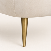 Hardware | detailed view of a tapered gold-finish metal loveseat leg beneath cream-beige velvet