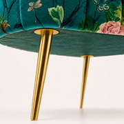 Hardware close-up | tapered gold metal legs and round underside attachment plates against the teal upholstered base