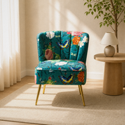 Warm room | teal-blue floral velvet armless slipper chair on a plain oatmeal rug beside a round oak table and lamp