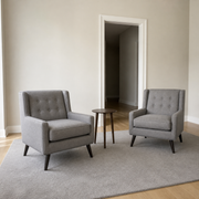 In scale | two gray tufted armchairs beside a fully open interior doorway with a dark hallway beyond