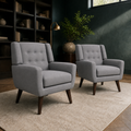 Library | two gray tufted armchairs on a cream rug in a deep green room with dark bookcases and a high window