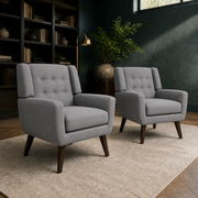 Library | two gray tufted armchairs on a cream rug in a deep green room with dark bookcases and a high window