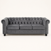 Front | Straight-on studio view of the light gray velvet Chesterfield sofa with three cushions, tufted back, nailhead trim, and black turned legs