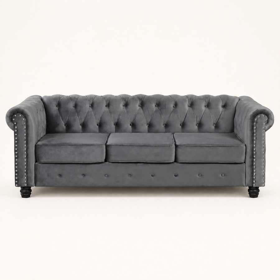 Front | Straight-on studio view of the light gray velvet Chesterfield sofa with three cushions, tufted back, nailhead trim, and black turned legs