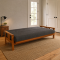 Scale | Futon opened flat into its bed position in a guest room, with the charcoal-gray mattress, wood frame, and glass-panel doorway visible