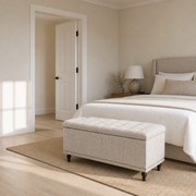 Scale view | warm beige tufted storage ottoman at the foot of a bed beside a full-height doorway