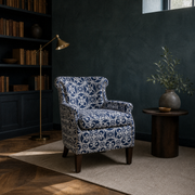 In a room | patterned club chair in a deep blue-green library with dark shelves and a cream rug