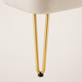 Hardware | macro of a slim gold metal hairpin leg with a black protective foot cap against ivory upholstery