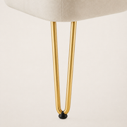 Hardware | macro of a slim gold metal hairpin leg with a black protective foot cap against ivory upholstery