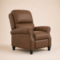 Studio three-quarter | brown faux-leather push-back recliner showing its side depth, padded back cushions, rolled arms, nailhead trim, and black bun feet