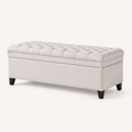 Studio | light gray polyester storage ottoman in a three-quarter studio view, showing the tufted flip top, plain side panel, rounded corner, and tapered dark wood legs