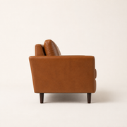 Side | Side profile of the mid-brown faux leather sofa with dark tapered legs