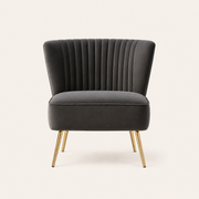 Front | Grey velvet accent chair with a flared channel-tufted back and four tapered gold legs on a clean studio ground
