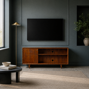 In a room | mahogany cherry TV stand against a deep blue-green paneled wall beneath a blank screen, with a brass lamp and plain rug