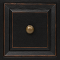 Hardware | macro of an antique brass-toned round knob on a distressed black recessed drawer panel