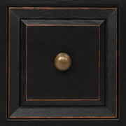 Hardware | macro of an antique brass-toned round knob on a distressed black recessed drawer panel