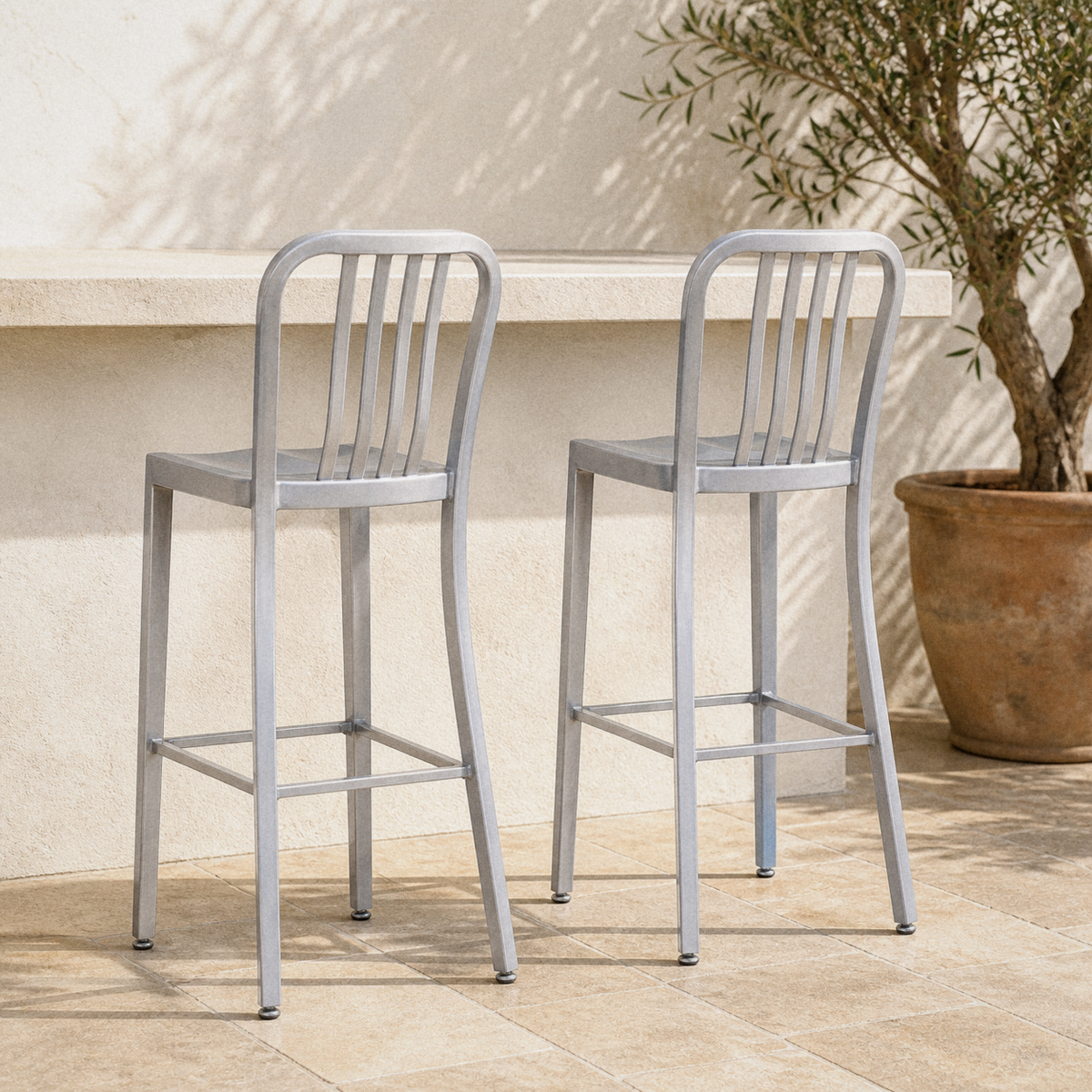 In a room | both silver slatted bar stools at an outdoor bar counter, limestone terrace with olive in terracotta
