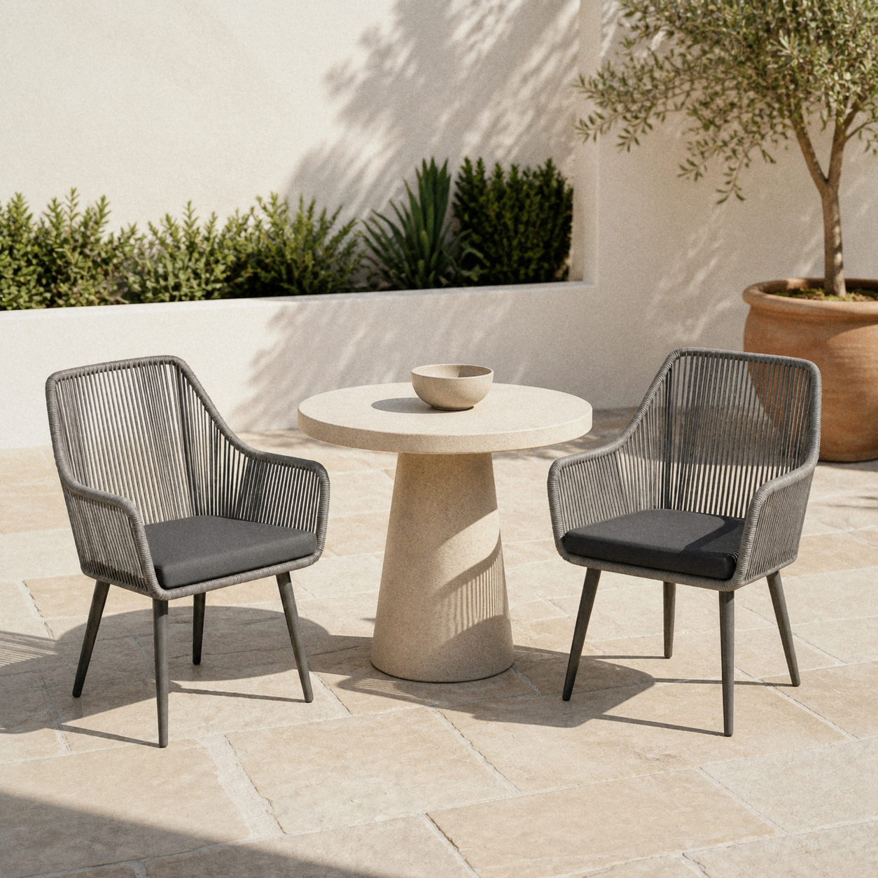 Room | two gray open-back polyethylene-wicker dining armchairs with gray seat cushions on a pale limestone terrace, olive in terracotta at right
