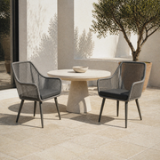 Room | the complete pair of two gray open-back wicker dining armchairs around a round dining table on a pale limestone terrace