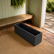 Garden veranda | empty matte charcoal-black composite trough planter on red-clay tile beside a timber bench