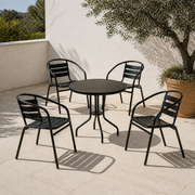 In a room | four black stacking patio armchairs around a round table on a sunlit limestone courtyard