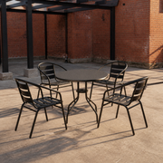In a room | four black stacking patio armchairs around a round table in a brick courtyard