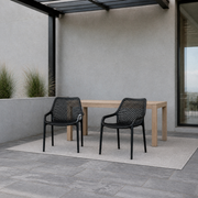 Cool coastal porch | Two matching Black perforated molded-plastic stacking chairs beside a pale wood table