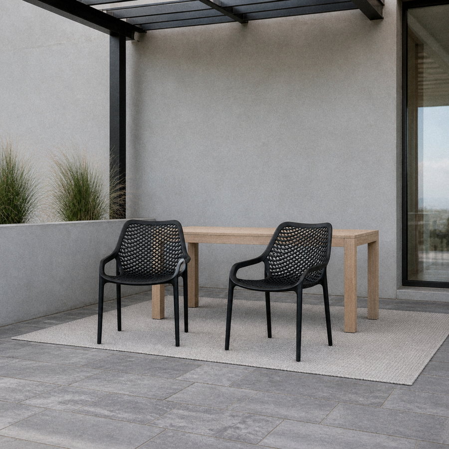 Cool coastal porch | Two matching Black perforated molded-plastic stacking chairs beside a pale wood table