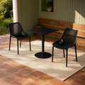 Garden veranda | Two Black perforated stacking chairs beside a black table and timber bench