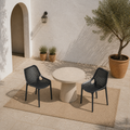 Mediterranean courtyard angle | Two Black perforated stacking chairs around a bare round stone table from above