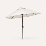 Studio three-quarter | open off-white octagonal umbrella showing canopy depth, vented crown, dark ribs, bronze pole and crank