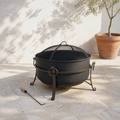 Sunlit limestone terrace | Dark steel cauldron fire pit with mesh spark screen and wood-handled poker