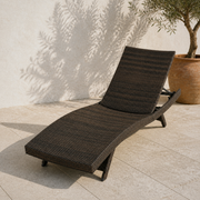 Angle | low three-quarter terrace view of the dark wicker chaise with olive tree behind