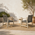 Terrace conversation view | Two light gray-washed acacia club chairs with dark open wicker backs facing a small styling table