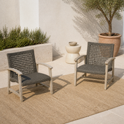 Complete pair | Two light gray-washed acacia club chairs with dark open wicker seats on a terrace
