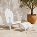 Terrace | White painted wood Adirondack chair and matching curved slatted ottoman on pale stone beside a potted olive tree