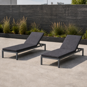 Rooftop garden | Two dark gray reclining chaise lounges on a concrete terrace with grasses