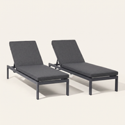 Studio front | Two dark gray reclining chaise lounges with raised backs on a warm white ground