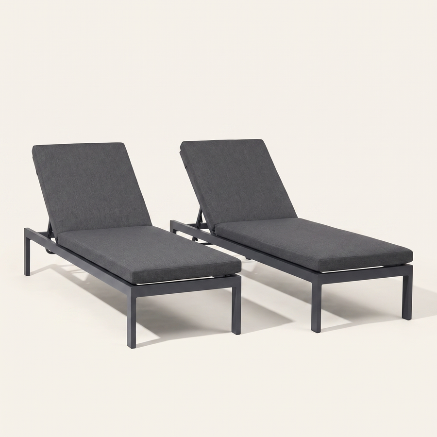 Studio front | Two dark gray reclining chaise lounges with raised backs on a warm white ground