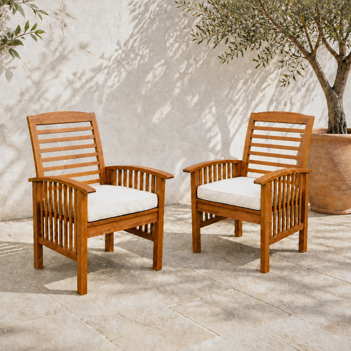 In a room | two warm-brown acacia dining armchairs with ivory seat cushions on a pale stone terrace beneath an olive tree
