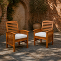 In a room | two warm-brown acacia dining armchairs with ivory seat cushions in a sunlit brick courtyard