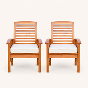 Front | pair of warm-brown acacia dining armchairs with ivory seat cushions facing forward on a clean studio backdrop